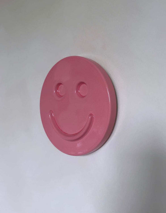 Pink ceramic artwork with a smiley face design against a light background.
