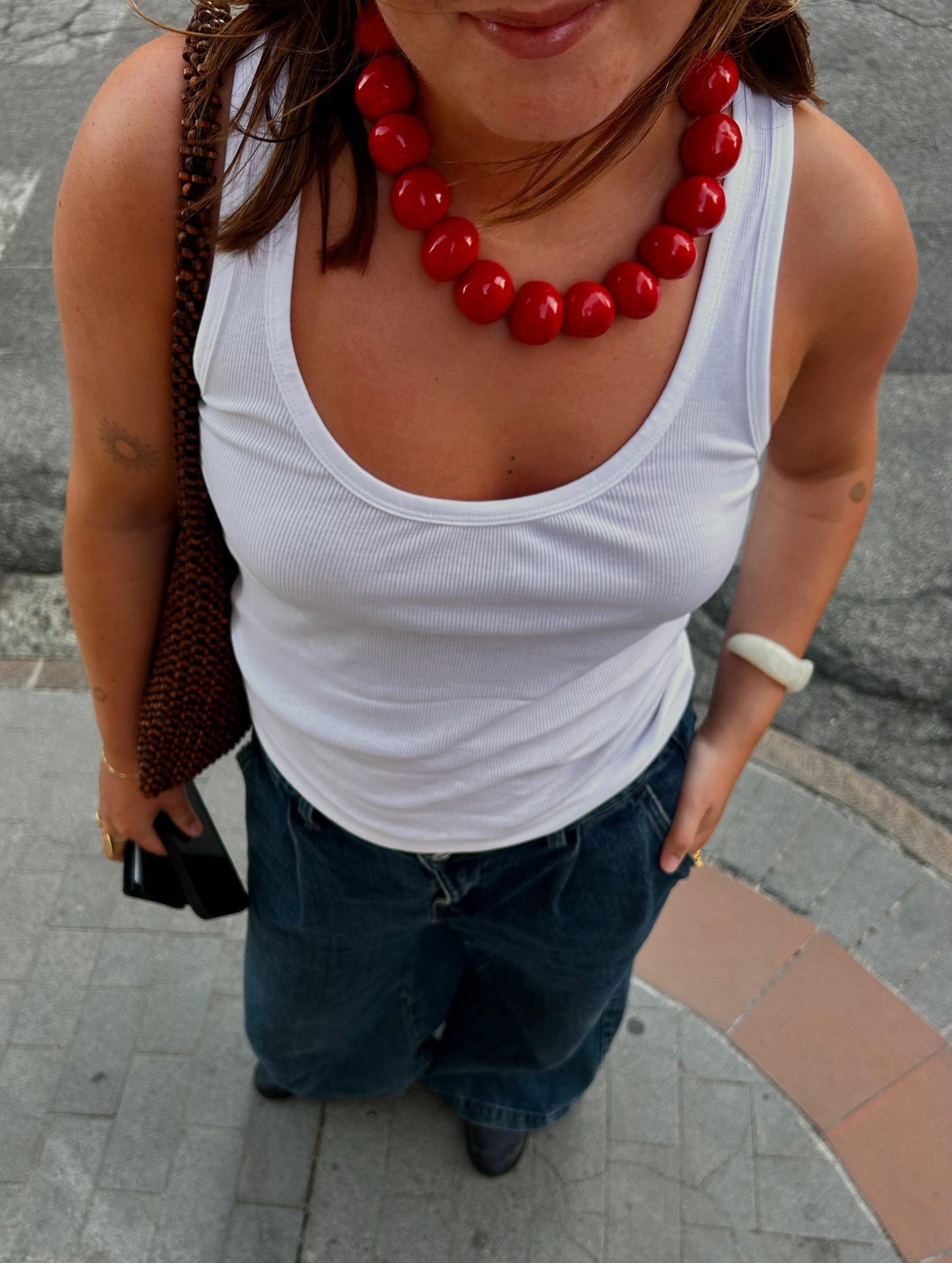 Handmade ceramic bead necklace with large glossy red beads worn with white tank top and denim jeans
