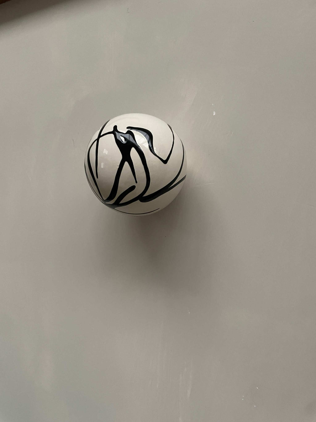 Ceramic ball wall sculpture with black swirl pattern.