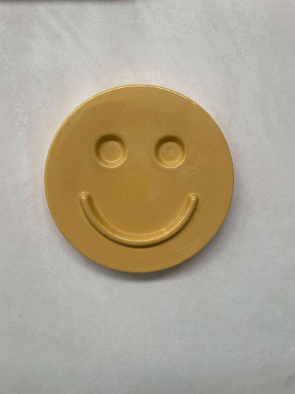 Yellow ceramic artwork with a smiling face.