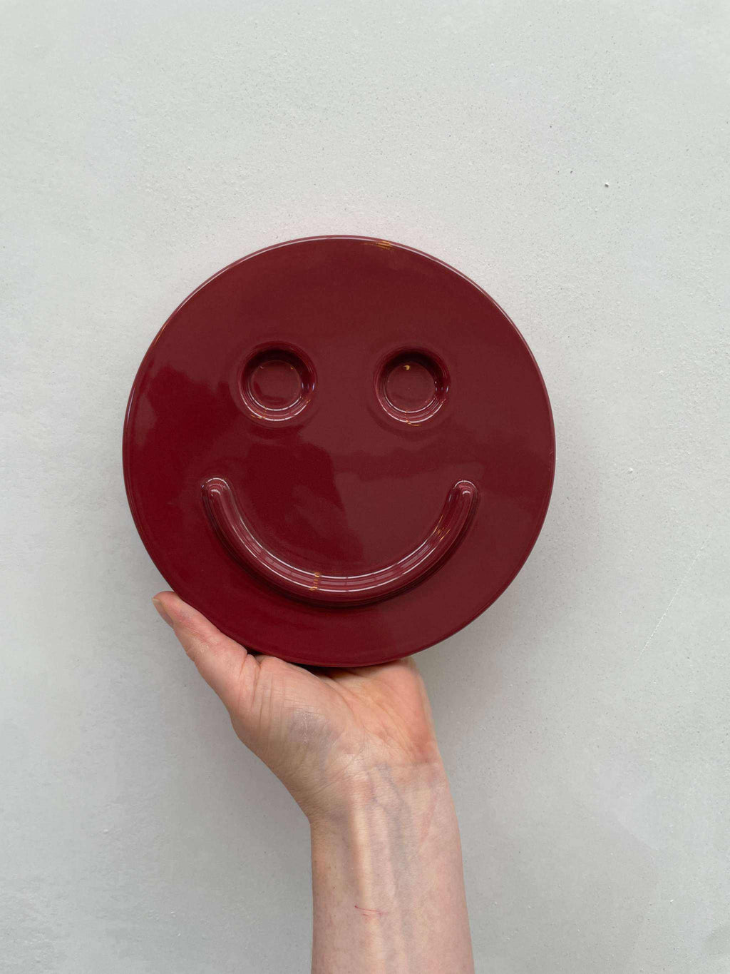 Burgundy ceramic artwork with smiley face design.