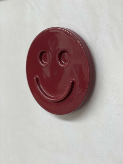 Burgundy ceramic artwork with a happy face design.
