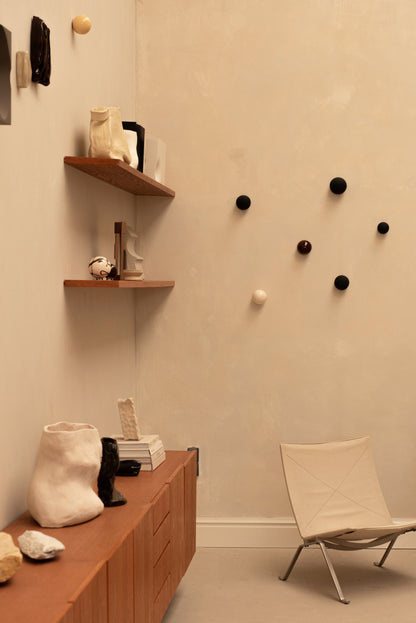 Handcrafted unique ceramic vase object displayed on wooden cabinet in minimalist room with shelves and chair