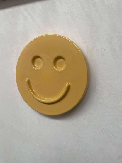 Yellow HAPPY ceramic artwork with a smiley face design.