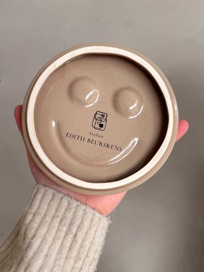 HAPPY ceramic wall art handmade round beige ceramic piece with smiley face indentations by Edith Beurskens