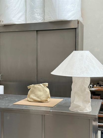 Handcrafted unique ceramic vase object on table with sculptural white lamp in studio setting