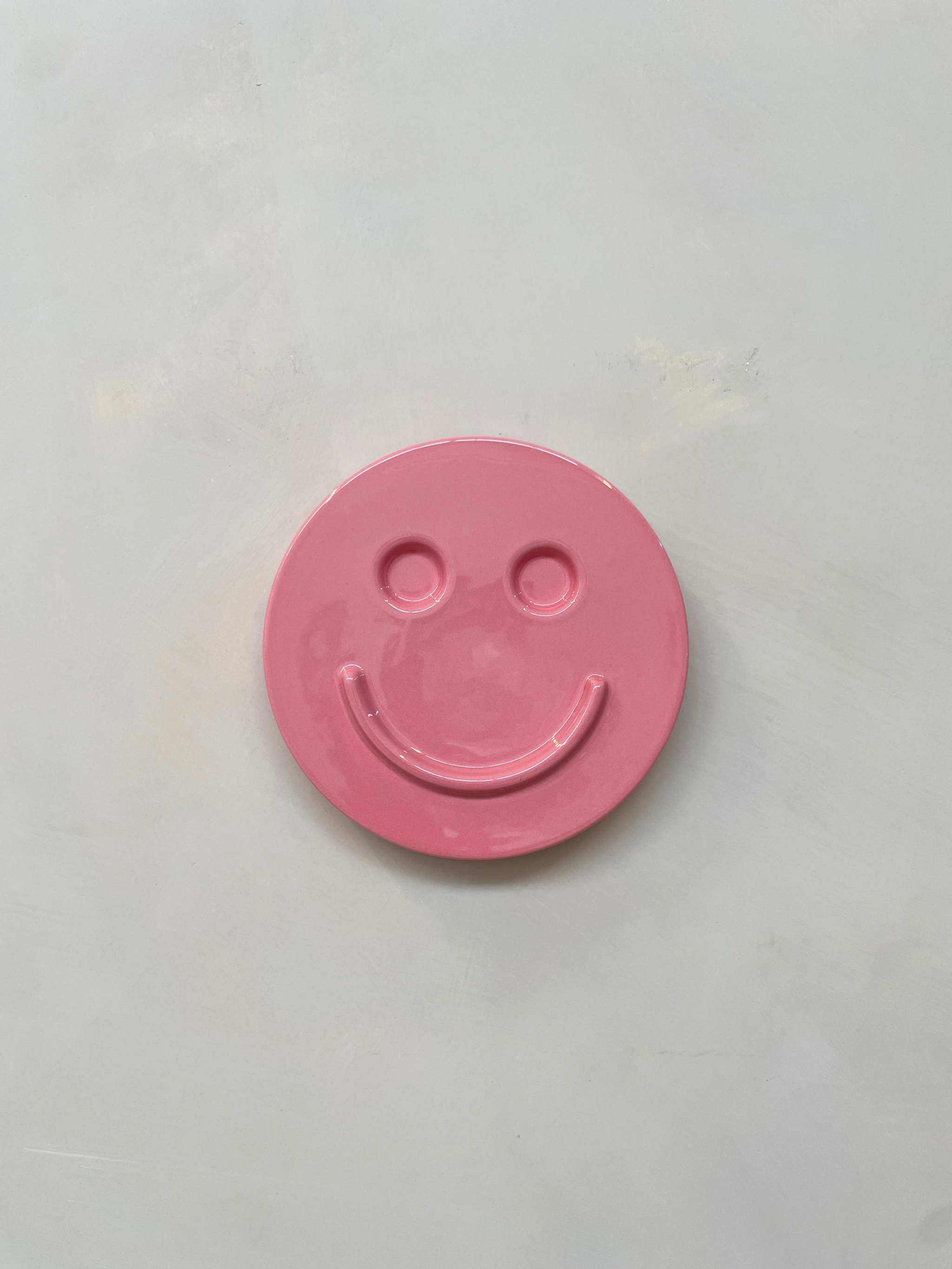 Pink ceramic smiley face artwork titled "HAPPY" by Edith Beurskens.