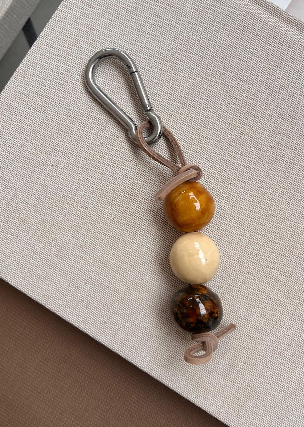 Handcrafted ceramic keychain with three natural-tone ceramic beads on a light brown leather cord and silver carabiner hook