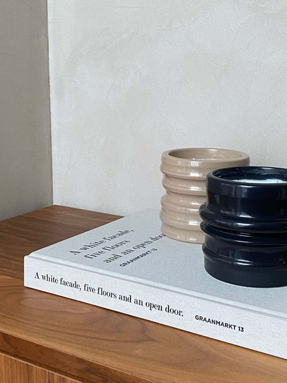 Scented candle holders from the Shapes Collection by Royal Goedewaagen, featuring design by Edith Beurskens, resting on a book titled "Graanmarkt 13".