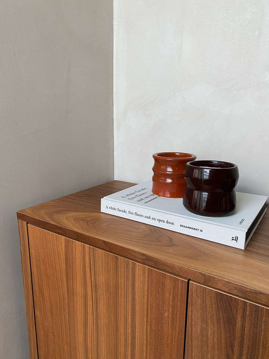 Scented candle holders from the Shape 01.02 Terra collection displayed on a wooden cabinet.
