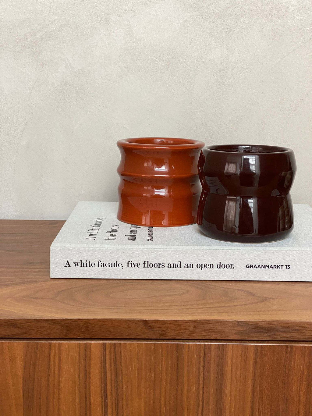 Scented candles in aubergine ceramic holders, featuring Shape 02 design, displayed on a wooden surface with a book.