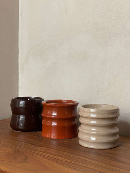 Scented candles Shape 04.01 Stone from the Royal Goedewaagen x L'AIMÉ collaboration in brown, orange, and beige ceramic holders on a wooden surface.