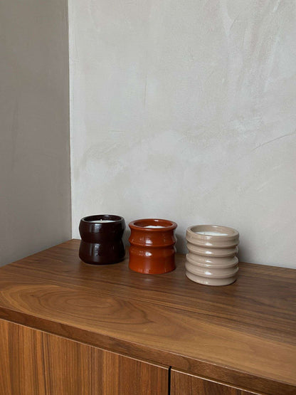 Scented candles in unique handcrafted ceramic holders on a wooden surface, part of the Shape 01.02 Terra collection.