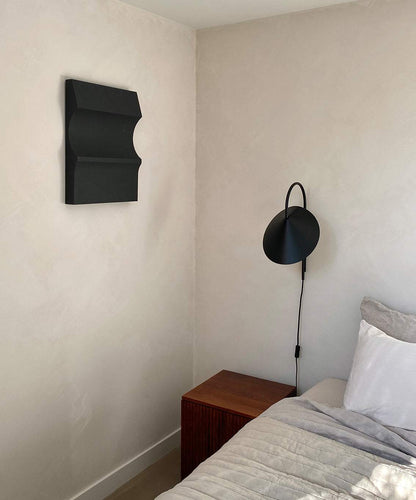 3D art piece '#22.03 Cécé' on a wall above a wooden nightstand in a minimalist bedroom setting.