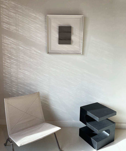 Vintage frame artwork by Edith Beurskens on wall with chair and black table.