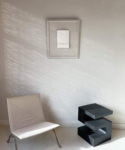 Vintage frame on wall, casting shadows, with chair and modern side table below.