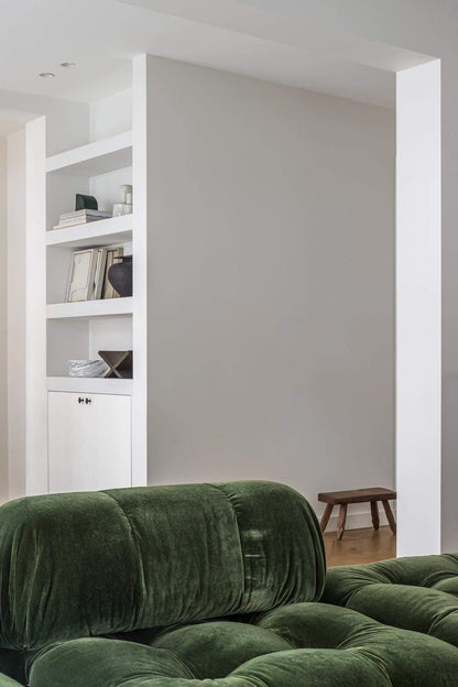 Green velvet sofa in a modern minimalist interior with white shelving.