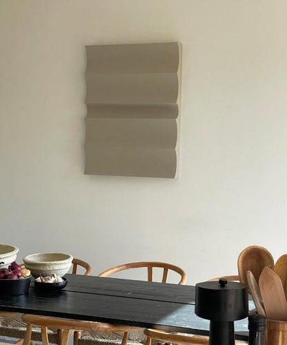 3D art wall piece in neutral tones with sand texture, displayed above a dining table.