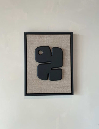 Canvas Noa artwork with anthracite black frame and textured plaster finish on a beige background.