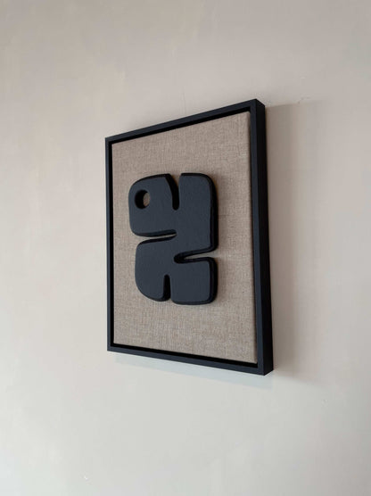 Canvas Noa with anthracite black artwork on a textured plaster surface, framed in anthracite black, 43 x 33 cm.
