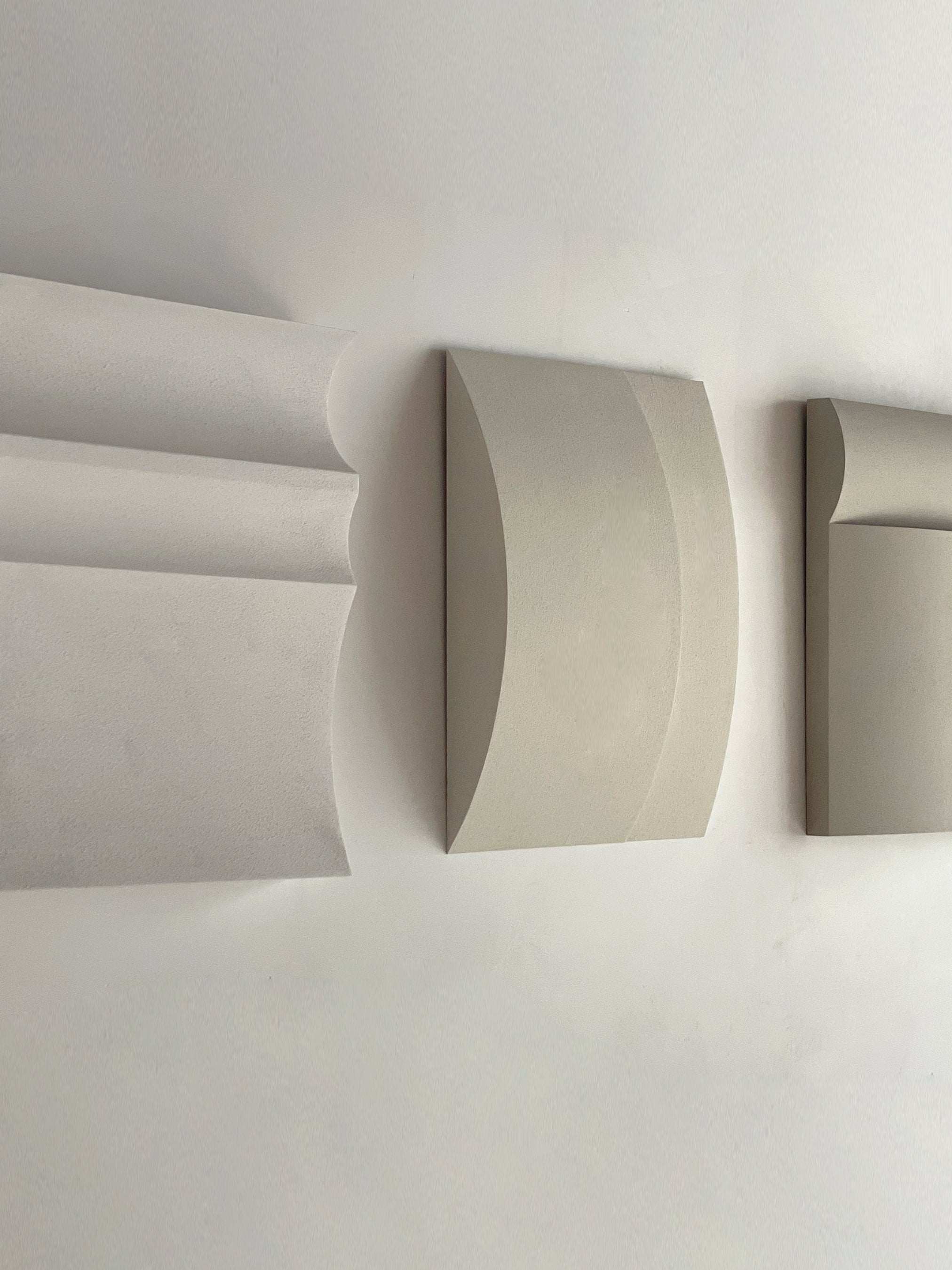 Contemporary wall art in white, shadow white, dark lime, brown wood, and mud grey tones displayed on a wall.